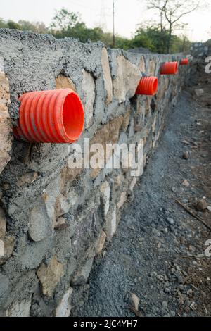 Una fila di colverti arancioni o tubi di uscita dell'acqua attraverso un muro di contenimento di pietra per il drenaggio delle tempeste nelle colline di Uttarakhand India. Foto Stock