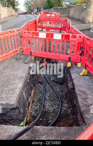 Barriere intorno a un buco parzialmente riempito in una strada per posare nuovi cavi elettrici Foto Stock