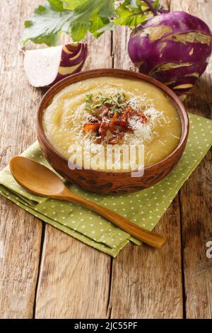 Zuppa Kohlrabi cremosa con pancetta e parmigiano in una ciotola sul tavolo. Verticale Foto Stock