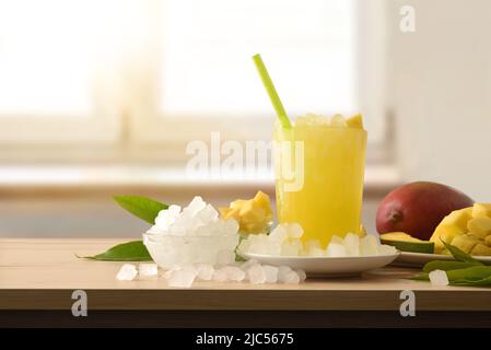 Sfondo con particolare di mango drink con un sacco di ghiaccio su tavola di legno con frutta e una ciotola con ghiaccio e sfondo finestra. Vista frontale. Orizzontale c Foto Stock