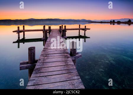 Holzsteg am Pfäffikersee im Gegenlicht bei Sonnenaufgang mit Blick zum Bachtel und Glärnisch im Hintergrund, Pfäffikon, Kanton Zürich, Schweiz Foto Stock