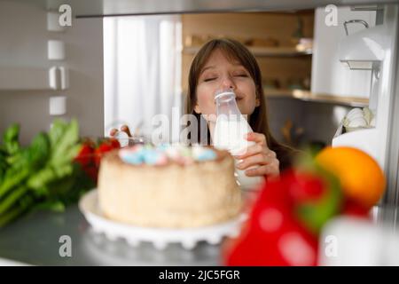 La ragazza sniffa il latte dalla bottiglia che ha preso nel frigorifero Foto Stock