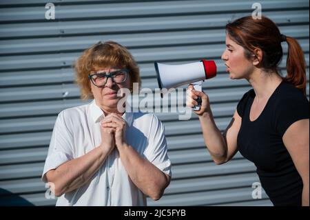 Il conflitto delle generazioni. Una donna arrabbiata di mezza età grida a una madre anziana attraverso un megafono. Una figlia adulta urla a un infelice Foto Stock
