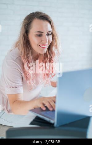 Una donna amichevole suona il pianoforte elettronico e conduce un video blog sul suo laptop. Rimani a casa. Insegnante di strumenti musicali. Musica di apprendimento a distanza Foto Stock