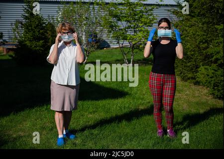 Mamma e figlia hanno messo su maschere mediche osservando la distanza sociale. Due donne sono in piedi nel parco ad una grande distanza da un amico. Contro il Foto Stock