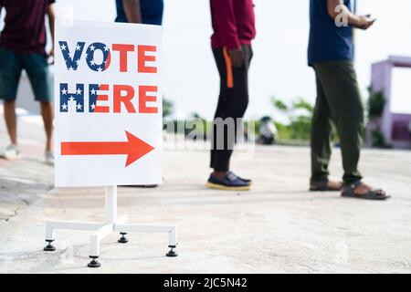 Le persone in fila in attesa di casting voto vicino al seggio elettorale votano qui cartello - concetto di diritti, responsabilità e democrazia. Foto Stock