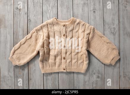 Pullover marrone lavorato a maglia, maglione di colore beige su sfondo di legno. Farment di Kid, vestiti per bambini, abbigliamento invernale autunnale.Woolen. Cardigan. Foto Stock