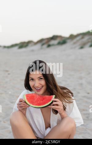 Donna allegra in camicia con cocomero maturo sulla spiaggia Foto Stock