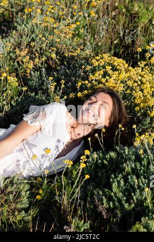 Donna allegra in abito bianco adagiata su prato con fiori gialli Foto Stock