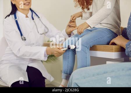 Specialista di neurologia che esamina il bambino piccolo e usando il martello per testare il riflesso del ginocchio Foto Stock