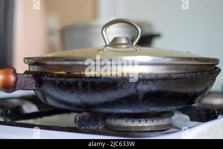 Tostatura di patate fresche in una padella in ghisa con olio di girasole. Una vista su una stovetop con una padella piena di patate fritte dorate in un vero e proprio Foto Stock