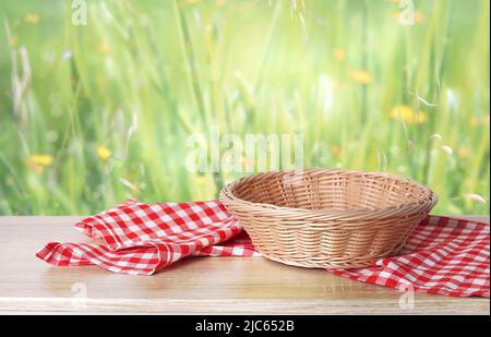 Cestino di paglia vuoto decorato con asciugamano da cucina a scacchi sul tavolo con sfondo verde naturale. Foto Stock