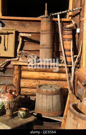 Sistemazione di vecchi oggetti popolari tradizionali all'esterno di un fienile in Romania. Briciolle di burro di legno. Foto Stock