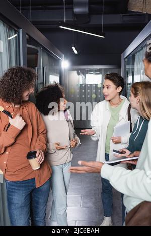 allegri studenti interrazziali gesturando mentre parlano nel corridoio dell'università Foto Stock