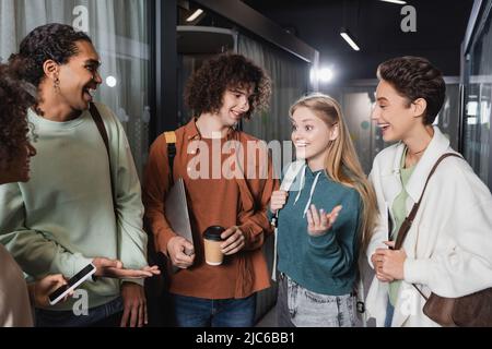 allegri studenti multiculturali che parlano e gesturano nel corridoio universitario Foto Stock