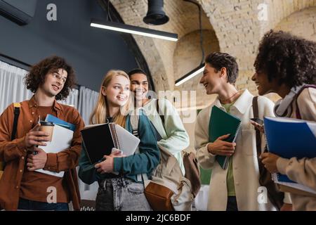 gruppo di giovani studenti interrazziali con taccuini e gadget che si guardano l'un l'altro all'università Foto Stock