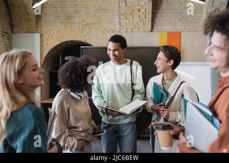 sorridente studente afroamericano che tiene un taccuino vuoto vicino ad amici multietnici Foto Stock