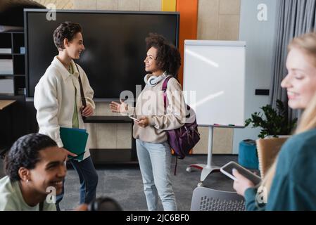 felice studente afroamericano con zaino che parla con un amico vicino a compagni di classe multietnici Foto Stock