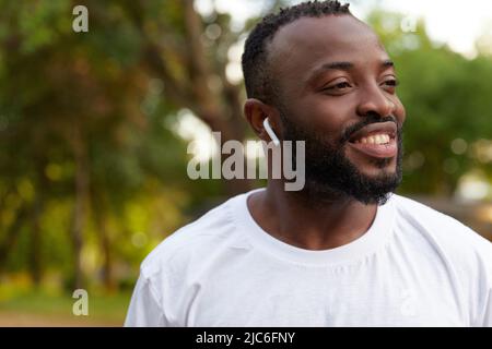 Sorridente uomo afroamericano adulto che cammina nel parco indossando le cuffie Foto Stock