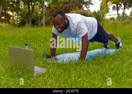 Felice giovane uomo adulto nel parco che ha un corso di formazione online. Stile di vita sano. Foto Stock