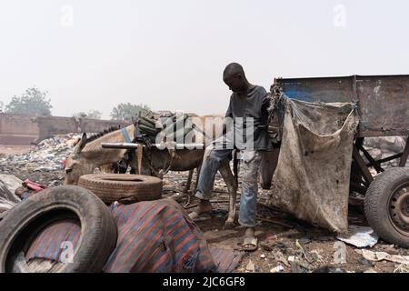 Giovane ragazzo africano senza speranza seduto da solo su una carretto con un asino, raccogliendo rifiuti e rifiuti per la rivendita. Concetto di povertà per i bambini africani Foto Stock