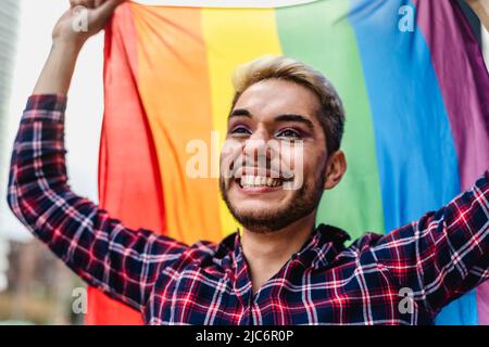 Un uomo gay felice che celebra il festival dell'orgoglio con la bandiera arcobaleno simbolo della comunità LGBTQ Foto Stock