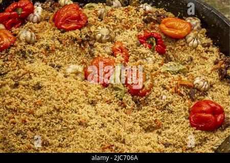 Cucina tradizionale orientale nazionale sotto forma di pilaf cucinato con verdure in un grande calderone in ghisa. Foto Stock