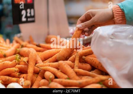 Primo piano delle mani delle donne che raccolgono le carote fresche in una borsa di cellophane nel negozio. Cibo delizioso e sano Foto Stock