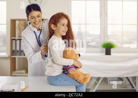 Pediatra femminile ascolta il battito cardiaco e i polmoni applicando stetoscopio alla parte posteriore della bambina. Foto Stock