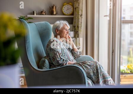 Donna anziana seduta in poltrona in casa sua Foto Stock