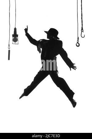 Una ballerina femminile è visto ballare sul palco. Vestita con abiti da uomo e con un cappello da uomo, si vede saltare a mezz'aria come una silhouette. Foto Stock