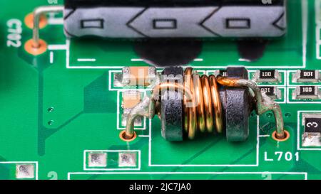 Dettaglio PCB verde. Bobina elettromagnetica e componenti elettronici a montaggio superficiale. Primo piano dell'induttore con filo di rame su nucleo di ferrite. Elettrotecnica. Foto Stock