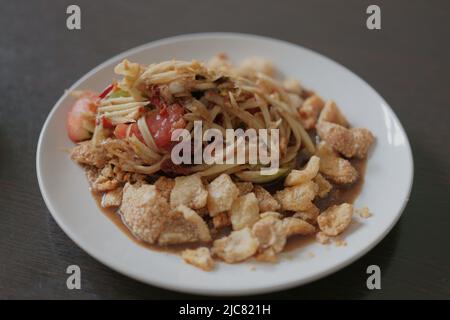 Delizioso Som Tam -insalata di papaya verde thailandese con fagioli verdi, pomodori, spuntino di maiale. Cibo di strada thailandese Foto Stock