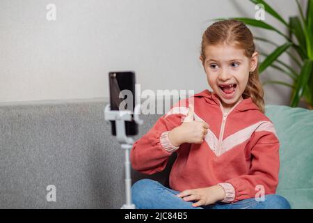 Piccola bionda blogger ragazza, una persona influente, comunica con gli abbonati, conduce una trasmissione dal vivo con un gatto, guarda lo schermo dello smartphone Foto Stock