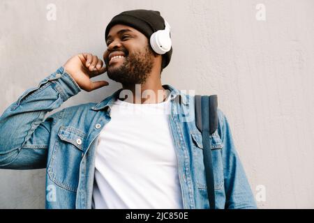 Giovane uomo nero che sorride e ascolta musica con le cuffie all'aperto Foto Stock
