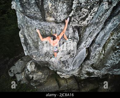 Giovane arrampicatore arrampicarsi su un percorso difficile su un'alta roccia con corda. Arrampicata su roccia senza paura durante il giorno d'estate. Concetto di sport estremo, avventure e stile di vita attivo. Vista aerea. Foto Stock