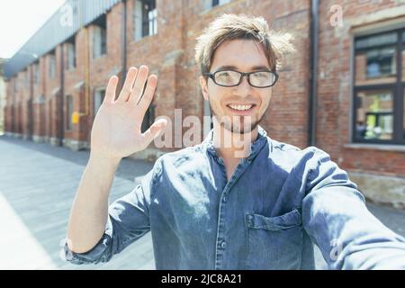 Un giovane bel blogger maschio con occhiali cammina per la città in esecuzione il suo video blog. Cammina lungo la strada e si spara in video Foto Stock