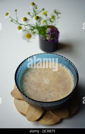 Cacao in una grande ciotola blu sul tavolo con un bouquet di camomilla. Foto Stock