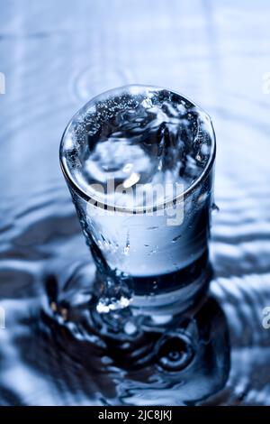 Immagine monocromatica blu di spruzzi d'acqua in un vetro. Foto Stock