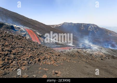 Etna-Colata di lava incandescente che scorre sul vulcano di Sicilia nella Valle del Bove con fumo e canale di scorrimento lavico Foto Stock