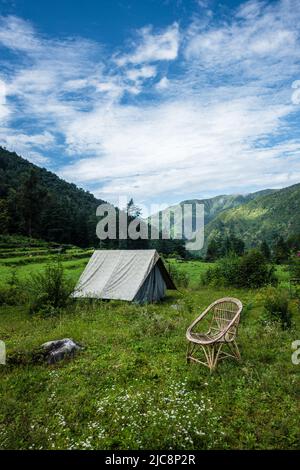 Un luogo turistico nei prati con un campo e una sedia di bambù con montagne sullo sfondo. Uttarakhand India. Foto Stock