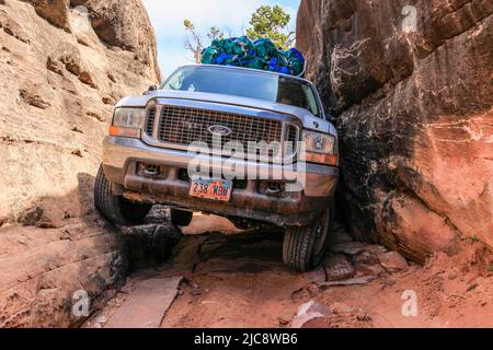 Un SUV a 4 ruote motrici si snoda attraverso lo stretto Squeeeze Box sul sentiero Elephant Hill. Canyonlands National Park, Utah. Come arrivare attraverso la Sq Foto Stock