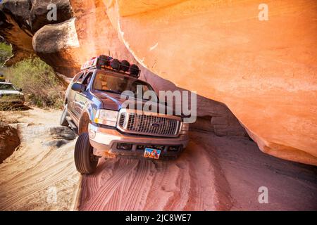 Una guida turistica attraversa un SUV a 4 ruote motrici attraverso una sezione stretta sotto una roccia nel Lavender Canyon, Utah. Il Canyon della lavanda è negli aghi D. Foto Stock