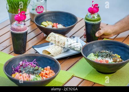 Man mano prendere una tazza di carta con vegan verde frullato in un caffè alla moda all'aperto Foto Stock