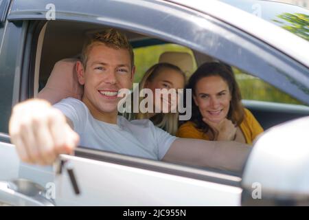 Uomo caucasico acquistare auto nuove o affittare e mostrando la chiave, seduto in auto. Foto Stock