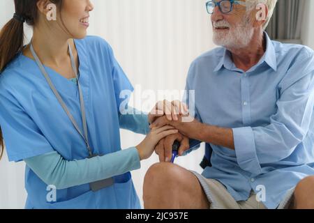 Infermiera asiatica seduta su un letto d'ospedale accanto ad un uomo più anziano che aiuta le mani, cura. Cura del paziente anziano e stile di vita di salute, concetto medico. Foto Stock