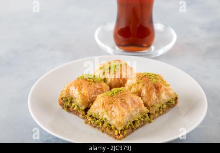 Pistacchio baklava su un piatto bianco con tè turco. Tradizionale baklava turco e tè su sfondo bianco Foto Stock