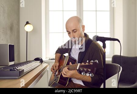 Concentrato musicista di talento maschile che stuccia corde sulla chitarra acustica creando nuova musica. Foto Stock