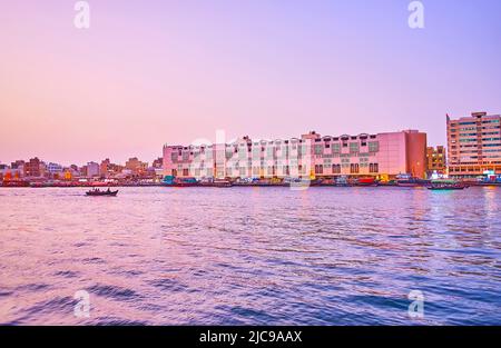 Goditi lo splendido crepuscolo viola sul Dubai Creek con vista su una barca galleggiante abra e sull'abitazione di Deira, Dubai, Emirati Arabi Uniti Foto Stock