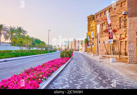 Passeggia lungo la strada panoramica al Seef con vista sulla tradizionale abitazione araba adobe, le colorate pansie sui aiuole e il luminoso cielo al tramonto, Dubai, Emirati Arabi Uniti Foto Stock